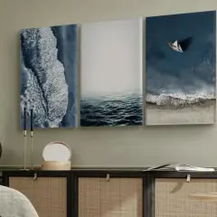 Un marco triptico con vistas al mar: olas rompiendo en la orilla, aguas tranquilas y un velero solitario.