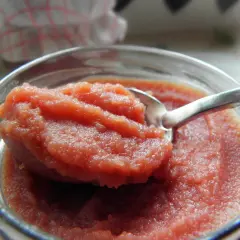 Łyżeczka zanurzona w słoiku z gęstym, różowym curd wiśniowym. Idealny dodatek do deserów.