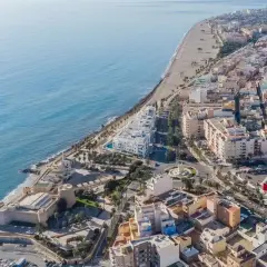Vista aérea de la costa de Almería, Roquetas de Mar, con el mar azul, la playa, edificios residenciales y un castillo histórico.