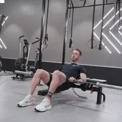 Man utför hip thrusters med skivstång på en bänk i ett modernt gym.