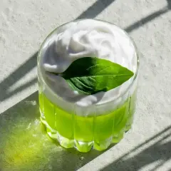 En grön thai basil drink med vitt skum och ett basilika-blad.