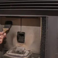 Main d'une personne nettoyant la chambre de combustion d'un poêle à pellet MCZ avec une brosse. Un problème de nettoyage peut causer des dysfonctionnements.