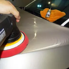 Nakładanie powłoki ceramicznej na lakier samochodu za pomocą polerki. Pomarańczowa ściereczka i butelka z preparatem K2.