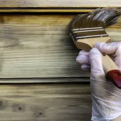 Application d'une lasure sur un bardage en bois, montrant la différence entre lasure et peinture. La lasure pénètre le bois, la peinture le recouvre.