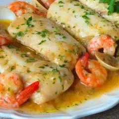 Merluza a la marinera con patatas, gambas y almejas en una salsa dorada.