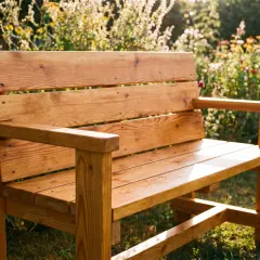 Eine **coole Gartenbank selber bauen** ist gar nicht schwer! Dieses Schmuckstück aus Holz steht im Sonnenschein inmitten blühender Blumen.