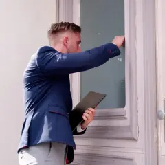 Mężczyzna w garniturze puka do drzwi, trzymając teczkę. Czy to wizyta komornika? Zastanawiasz się, ile może zabrać komornik?