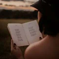 Kobieta czyta piękne wiersze o życiu, otoczona naturą o zmierzchu.