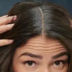 Mujer se toca el cabello oscuro, mostrando cómo disimular las canas en la raya.