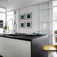 Isla de cocina moderna con encimera oscura, separada del salón por una pared de cristal.