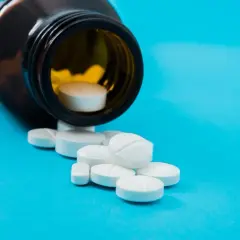 Białe tabletki, w tym jedna z nacięciem, wysypują się z brązowej butelki. To może być vicodin.