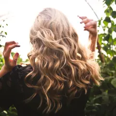 Kobieta z blond lokami w czarnej koronkowej bluzce na tle zieleni.
