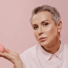 Femme aux cheveux gris et yeux marrons, maquillage subtil, tenant un objet rose.