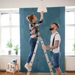 Coppia installa un lampadario, una delle migliorie che aumentano il valore di un immobile.