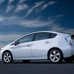 Biały Prius 3 zaparkowany nad wodą, pod błękitnym, chmurnym niebem.