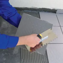 Układanie płytek na tarasie, tworząc płynne połączenie tarasu z domem. Ręka z kielnią rozprowadza klej.
