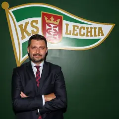 Marcin Kaczmarek, trener, stoi przed zieloną ścianą z logo Lechii Gdańsk.
