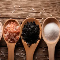 Cinco cucharas de madera muestran una composición de la sal: blanca gruesa, rosa del Himalaya, negra, fina blanca y con hierbas.