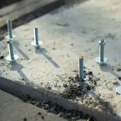 Kilka metalowych kotew z podkładkami i nakrętkami osadzonych w betonie.