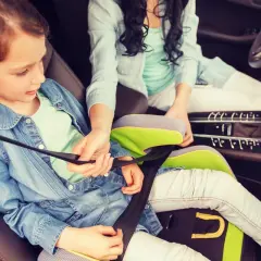 Ein Kind im Kindersitz wird angeschnallt. Die Frage "ab wann darf ein Kind vorne sitzen" ist hier relevant, da sie auf dem Beifahrersitz sitzt.
