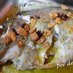 Un delicioso san martiño pescado al horno con ajo laminado y hierbas verdes, bañado en su jugo.