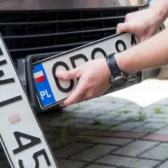 Ręce montują polską tablicę rejestracyjną. Nowe oznaczenie pojazdu gotowe do drogi.