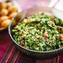 En skål med fräsch tabbouleh, perfekt för ett somrigt tabbouleh recept. Bredvid syns en bricka med små potatisar.