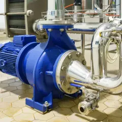 Pompe industrielle bleue connectée à des tuyaux en acier inoxydable. L'ensemble est conçu pour gérer des fluides sous haute pression.