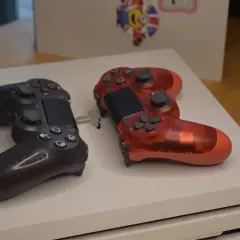 Dwa kontrolery, czarny i przezroczysty czerwony, leżą na białej konsoli PS4. Pamiętasz, kiedy wyszło PS4?