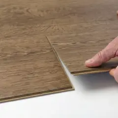 Close-up of a hand performing vinyl floor installation, clicking two wood-look planks together.