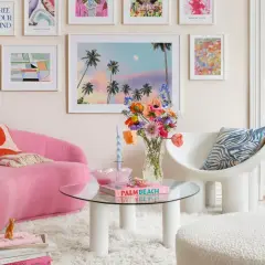 Ein Wohnzimmer im **danish pastel** Stil mit einem pinken Sofa, bunten Bildern und einer Vase voller Blumen.