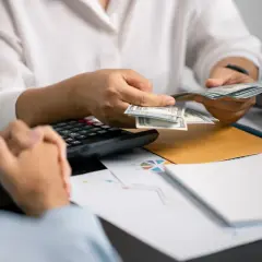 Osoba liczy pieniądze, kalkulator i dokumenty na stole. Czy to umowa o dzieło, czy sprawa z komornikiem?
