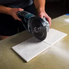 Hands carefully cutting decorative porcelain tile with an angle grinder, creating a clean line.