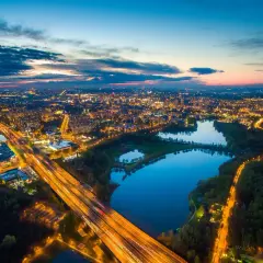 Widok z lotu ptaka na miasto nocą, z oświetloną autostradą i trzema stawami odbijającymi światła.