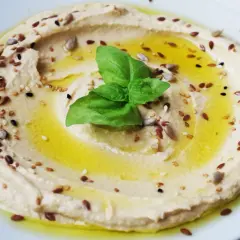 Hummus di ceci cremoso, condito con olio d'oliva, semi misti e una foglia di basilico. Perfetto da gustare con pane pita o verdure fresche.