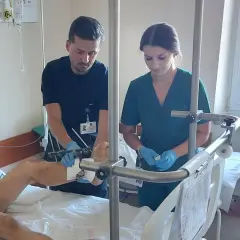Lekarze w szpitalnej sali badają nogę pacjenta z aparatem zewnętrznym.