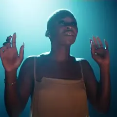 Cynthia Erivo stand up, wznosi ręce w górę, w świetle reflektorów.