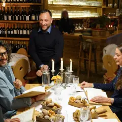 Un gruppo di amici ride a tavola in un ristorante di Milano, tra candele e bottiglie di vino.