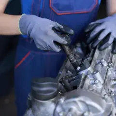 Mecánico con guantes ajusta una pieza del motor, posiblemente relacionada con el cigüeñal de motor.