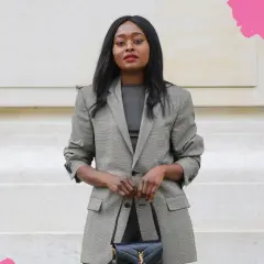 Eine Frau im karierten Blazer und schwarzer Tasche zeigt, was ist business casual: schick und doch entspannt.