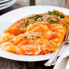 Väl förberedd grava lax med dill och peppar på en vit tallrik, redo att avnjutas.