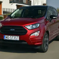 Czerwony Ford Ecosport w ruchu miejskim. Kierowca w okularach przeciwsłonecznych. Wiele pozytywnych ford ecosport opinie potwierdza jego miejski charakter.