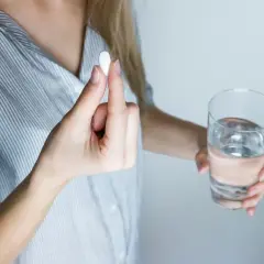 Donna tiene una pillola, forse un antibiotico per denti e gengive, accanto a un bicchiere d'acqua.