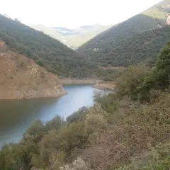 Embalse de Vallforners, un lago sereno rodeado de colinas verdes y rocosas, con vegetación densa en primer plano.