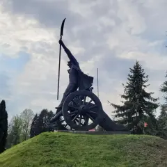 Pomnik Kościuszki w Racławicach, z kosynierem na armacie, pod pochmurnym niebem.