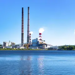 Elektrownia z kominami i chłodniami, odbijająca się w wodzie.