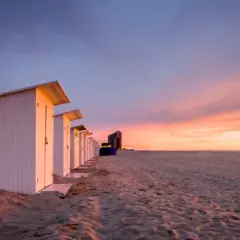 Strandkabinen am Meer bei Sonnenuntergang mit dramatischem Himmel.