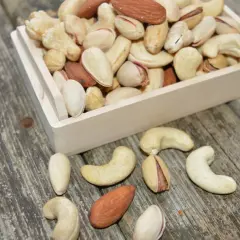 Drewniana skrzynka z orzechami: migdały, pistacje i orzechy nerkowca na drewnianym tle.