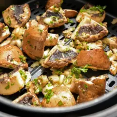 Pyszne pieczarki z airfryer, przyprawione i posypane natką pietruszki, gotowe do podania.
