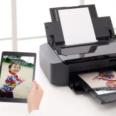 Uchwyć radość dziecka i ciesz się drukowaniem zdjęć w domu. Tablet pokazuje uśmiechniętą twarz, a drukarka właśnie wydrukowała podobne zdjęcie.